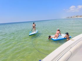 A fun day at the beach with friends enjoying paddleboarding and relaxing on a floating mat in the clear waters — perfect for summer adventures.
