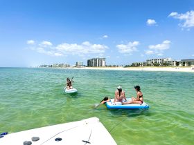 A fun day at the beach with friends paddleboarding and relaxing on inflatable mats in the clear waters — perfect for summer adventures.