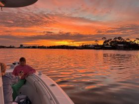 Two friends enjoy a beautiful sunset on a boat, capturing the moment with smiles and drinks — a perfect setting for relaxation and celebration on the water.