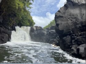 A stunning view of a waterfall cascading over dark rocks, surrounded by lush greenery — a perfect representation of nature's beauty and adventure on the water.