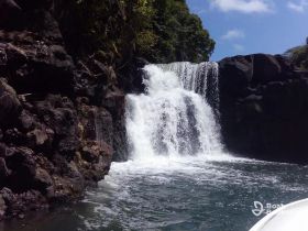 A stunning view of a waterfall cascading into clear waters, framed by lush greenery — a perfect highlight of a scenic boat tour.