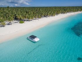 A stunning aerial view of a boat anchored in crystal-clear waters, surrounded by a pristine beach and lush palm trees, perfect for tropical getaways.