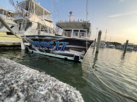 A close-up view of the 'Havoc II' boat docked at Virginia Beach, showcasing its sleek design and vibrant branding against the serene marina backdrop.