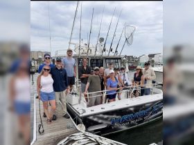 A lively group poses on the deck of the fishing boat 'Havoc II' in Virginia Beach, celebrating a successful fishing trip with their catch displayed in front.