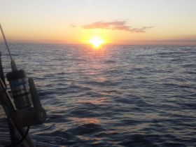 A stunning sunset over the ocean, captured from the deck of a boat, showcasing the tranquil beauty of evening on the water.