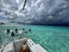 A group enjoys a refreshing swim in the stunning turquoise waters, with a boat anchored nearby and dramatic clouds in the background, perfect for a day of adventure on the water.