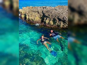 A couple enjoys snorkeling in crystal-clear waters near a rocky formation, showcasing the beauty of underwater adventures.