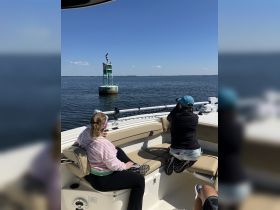 Two guests enjoy a scenic view from their boat, capturing the moment as they observe a buoy with birds perched on top — a perfect day on the water.