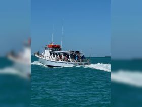 The Cora Beth boat is seen cruising through vibrant turquoise waters, filled with guests enjoying a lively day on the water.