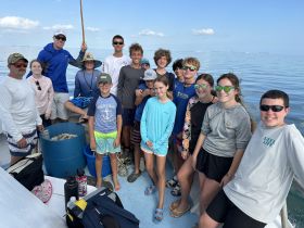 A cheerful group of kids and adults pose together on a boat, ready for a fishing adventure — perfect for family outings and group activities on the water.