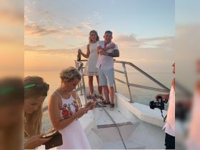 A lively group celebrates at sunset on a boat, enjoying champagne and capturing memories — perfect for unforgettable boat parties and gatherings.