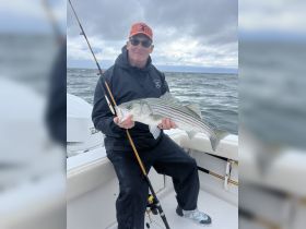 A proud angler holds up a freshly caught striped bass while fishing on a boat, showcasing the thrill of a successful day on the water.