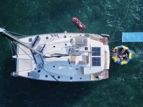 A lively group enjoys water activities around a catamaran, with a floating mat and jet ski nearby, capturing the essence of fun on the water.