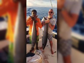 A joyful moment captured as two individuals proudly display their impressive catch while fishing on a boat, showcasing the thrill of a successful fishing trip.