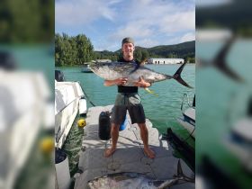 A proud angler holds up a large tuna catch on a dock, showcasing the thrill of fishing in beautiful waters — a perfect moment for fishing enthusiasts.