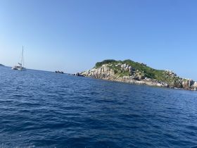 A picturesque view of a sailboat navigating the serene waters near a rocky island, showcasing the beauty of a day at sea.