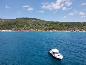 Aerial view of a boat navigating through crystal-clear waters near a lush coastline, showcasing the beauty of the surrounding nature.