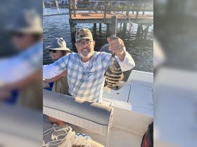 A man proudly displays his catch while fishing on a boat, capturing the joy of a successful day on the water with friends.