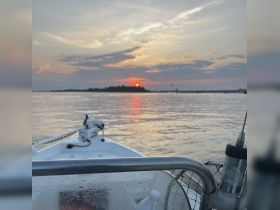 A serene sunset view from the bow of a boat, showcasing the tranquil waters and distant land — perfect for peaceful evening cruises.