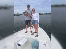 A couple proudly displays their catch while fishing on a boat, showcasing a fun day on the water.