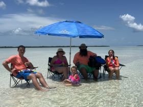 A joyful family enjoys a day at the beach on a sandbar, relaxing under an umbrella and playing in the shallow water — perfect for creating lasting memories together.