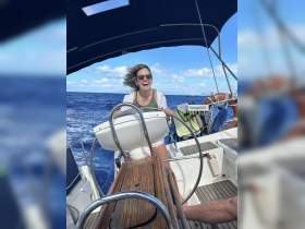 A joyful woman steers a sailboat through the ocean, capturing the thrill of sailing on a sunny day.