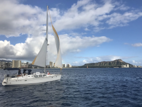 A sailboat navigates the waters near Diamond Head, with city views in the background — a perfect setting for a sailing adventure in Hawaii.