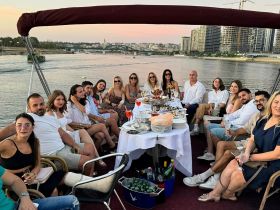 A lively group enjoys a dinner cruise on a boat, celebrating with cocktails and delicious food while taking in the scenic views.