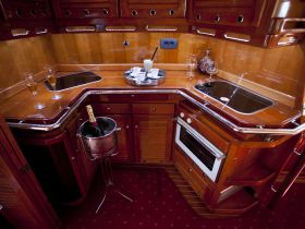 An elegant interior view of a boat's kitchen area featuring polished wood finishes, champagne glasses, and a well-equipped cooking space, perfect for onboard dining experiences.