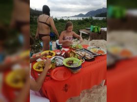 A group enjoys a delicious beachside meal with a variety of dishes laid out on a vibrant tablecloth, perfect for a tropical dining experience.