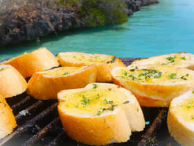 Delicious garlic bread grilling on a barbecue, perfect for a day on the water. Enjoy tasty onboard meals while soaking in the beautiful turquoise surroundings.