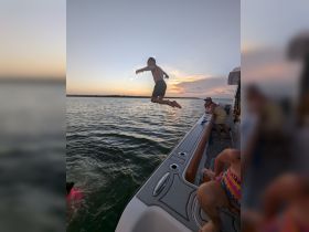 A child joyfully jumps off the side of a boat into the water at sunset, capturing the essence of summer fun and adventure on the water.