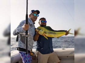 Two anglers proudly display their catch aboard a fishing boat, showcasing the thrill of deep-sea fishing in the open ocean.