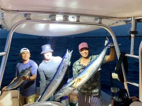 A group of friends proudly displays their catch during a nighttime fishing trip, showcasing the excitement of fishing adventures on the water.