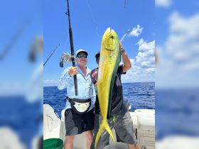 Two anglers proudly display their impressive catch of a dolphin fish while fishing at sea, showcasing the thrill of deep-sea fishing adventures.