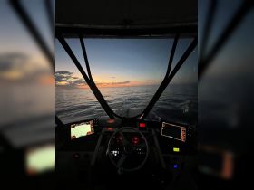 A stunning view from the helm of a boat at sunset, showcasing the navigational instruments and the serene ocean ahead — perfect for evening cruises.