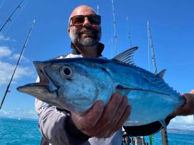 A proud angler displays his catch on a fishing trip, showcasing the thrill of deep-sea fishing in clear blue waters.