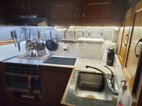 A well-equipped boat kitchen featuring a sink, stove, and hanging cookware, perfect for preparing meals while at sea.