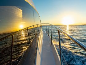 A stunning view from the front of a yacht as it glides through the water at sunset, showcasing the beautiful reflections and serene atmosphere.