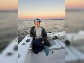 A joyful woman relaxes on the edge of a boat during sunset, capturing the essence of a perfect day on the water.