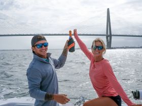 A joyful couple celebrates on a boat with champagne, showcasing the stunning backdrop of a bridge — perfect for memorable moments on the water.