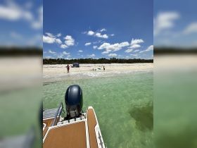 A family enjoys a sunny day at the beach, with a boat anchored nearby, perfect for a sandbar stop and fun in the water.