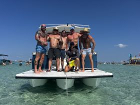 A group of friends enjoys a fun day on a pontoon boat, celebrating with drinks in the shallow waters — perfect for summer gatherings and beach parties.