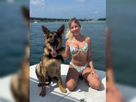 A young woman poses with her German shepherd on a boat, showcasing a joyful moment of human-animal interaction against a scenic water backdrop.