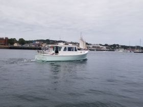 A charming lobster boat named 'Lobster Tales' navigates through calm waters, showcasing its unique design and functionality.