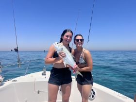 Two friends proudly display their catch while fishing on a boat, capturing the excitement of a successful day on the water.