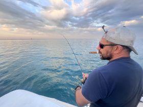 A man enjoys a peaceful fishing experience on the open ocean, complete with a cigar and stunning views — perfect for fishing enthusiasts seeking relaxation on the water.