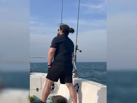 A man stands on a boat, focused on fishing in the open ocean, capturing the essence of a relaxing day on the water.