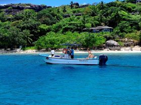 A scenic view of a boat cruising in crystal-clear waters, surrounded by lush tropical greenery and rocky formations, perfect for exploring island destinations.