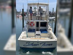 A fishing boat named 'Silver Tuna' is docked with two men preparing for a day on the water, showcasing the vessel's rear view and fishing gear.